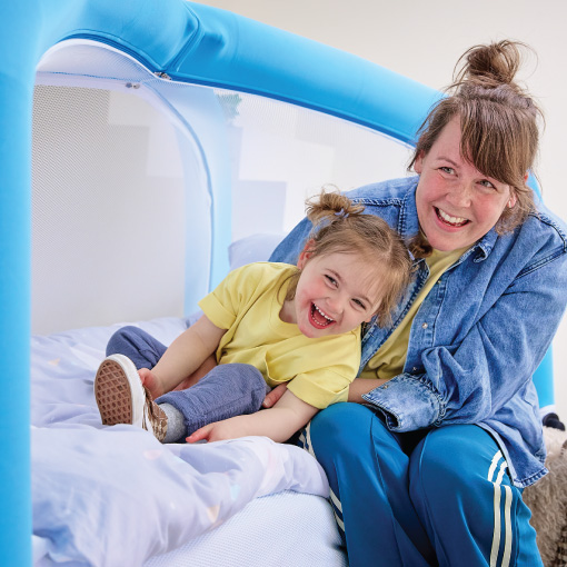Mother and young daughter laughing together on a blue inflatable play structure indoors.