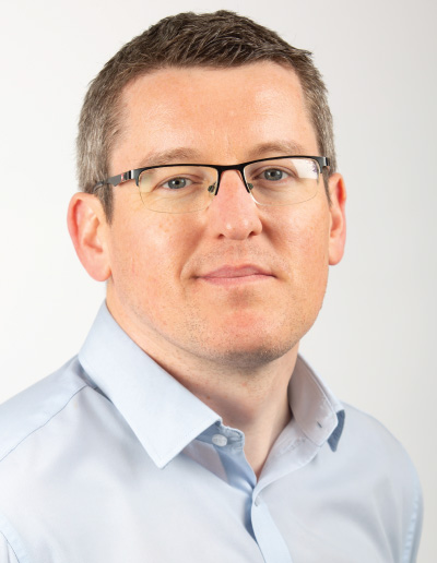 Stephen-photo-for-web Head-and-shoulders portrait of a man in a pale blue shirt and glasses, looking slightly to the right.